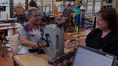 Senior using therapy equipment while therapist instructs her