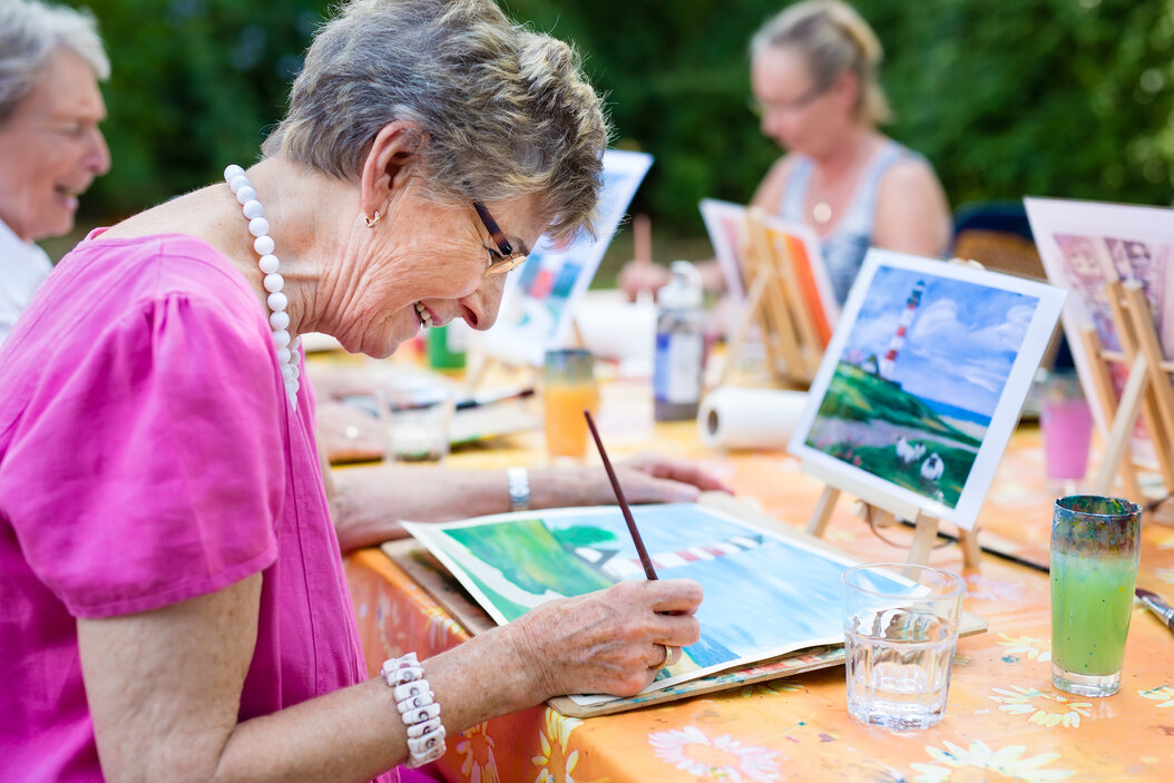 Senior woman smiling and painting with a group in the park