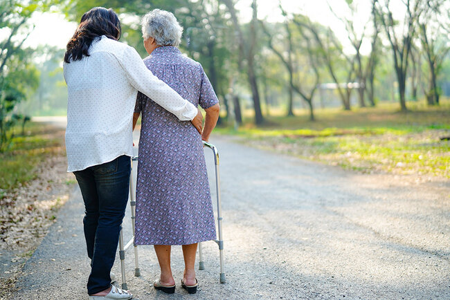 A woman helps care for an elderly woman walking outside