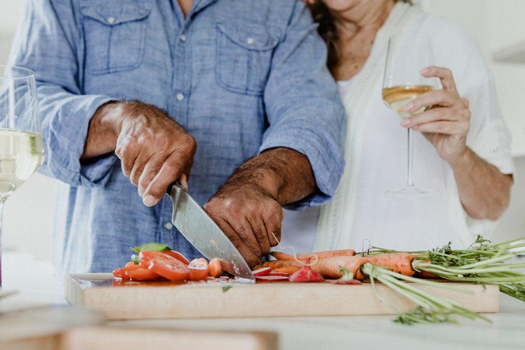 senior couple chopping vegetables to cook dinner while drinking white wine